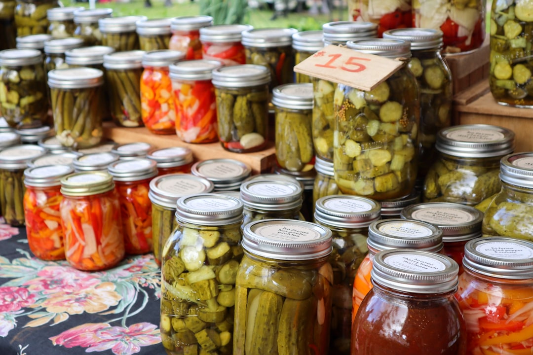 A farmers' market table covered in mason jars of pickles and fermented vegetables with a hand-written $15 price sign.