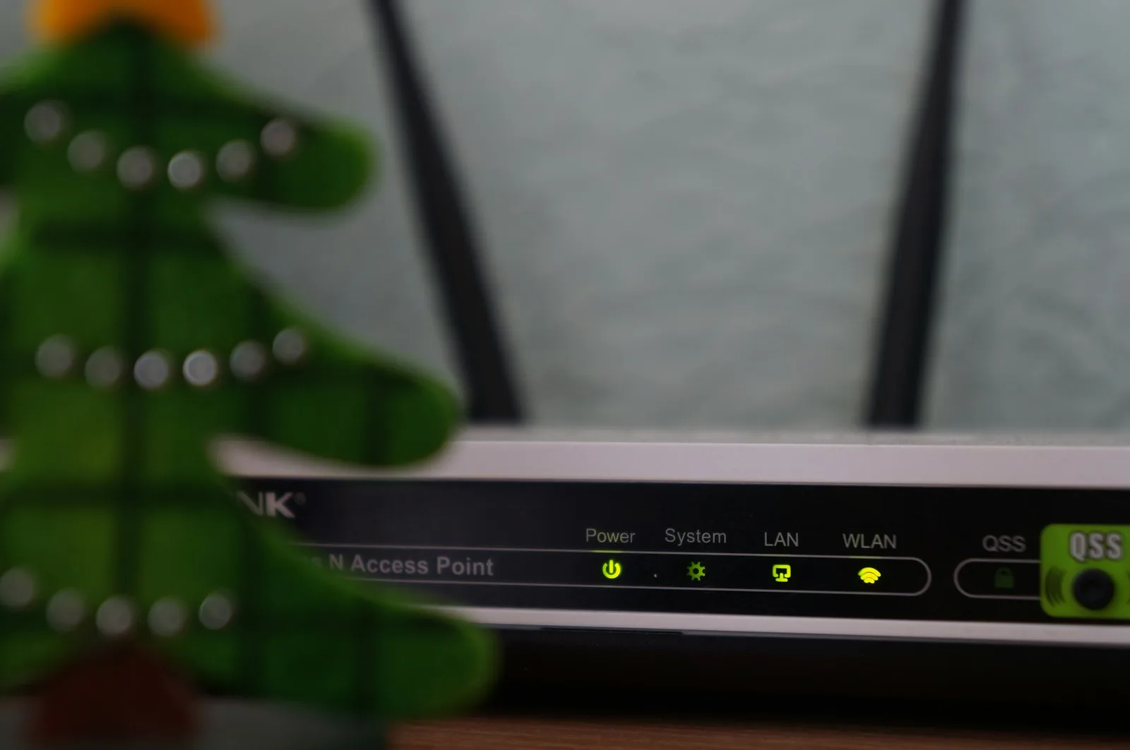 A compact single-board computer sitting beside a home router with glowing status lights on a wooden shelf, softly lit by window light