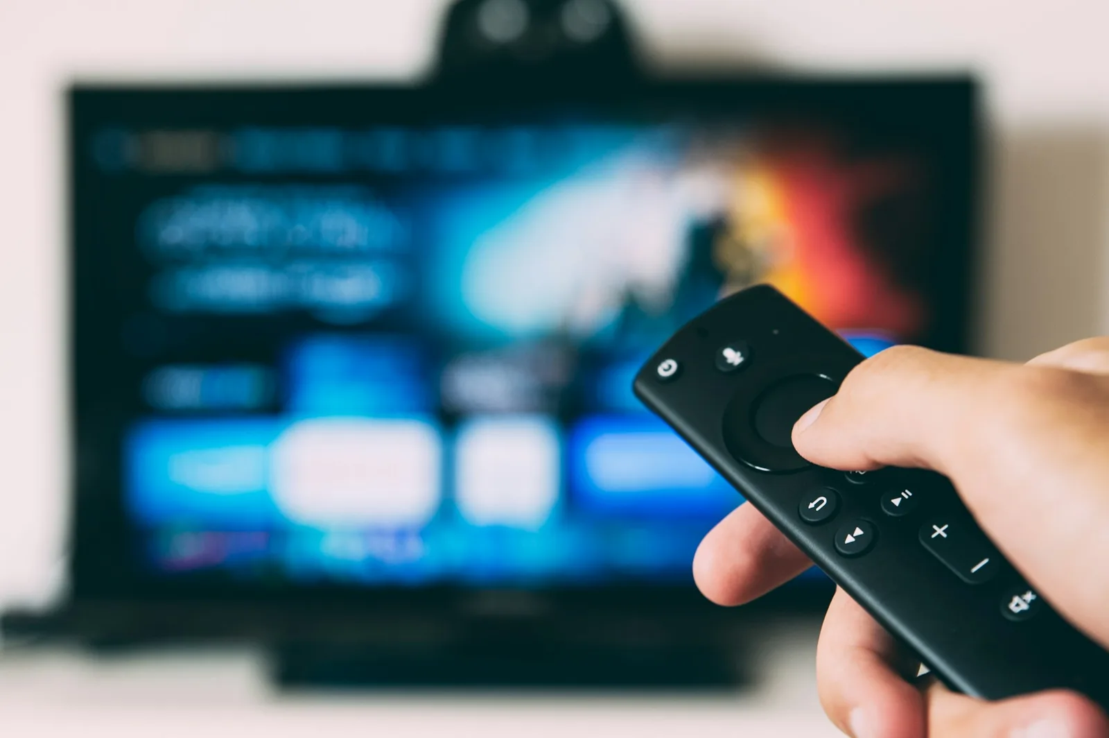 A smartphone and a TV remote control resting on a coffee table in a dim living room, with a glowing television screen blurred in the background