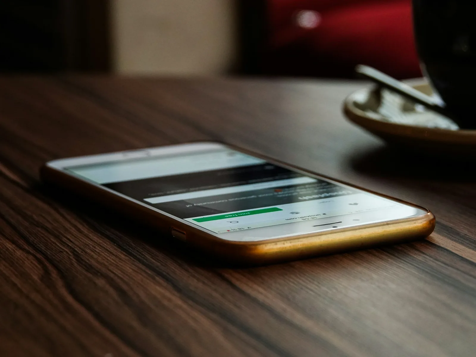 A smartphone on a wooden table showing a login screen, laptop open blurred in the background