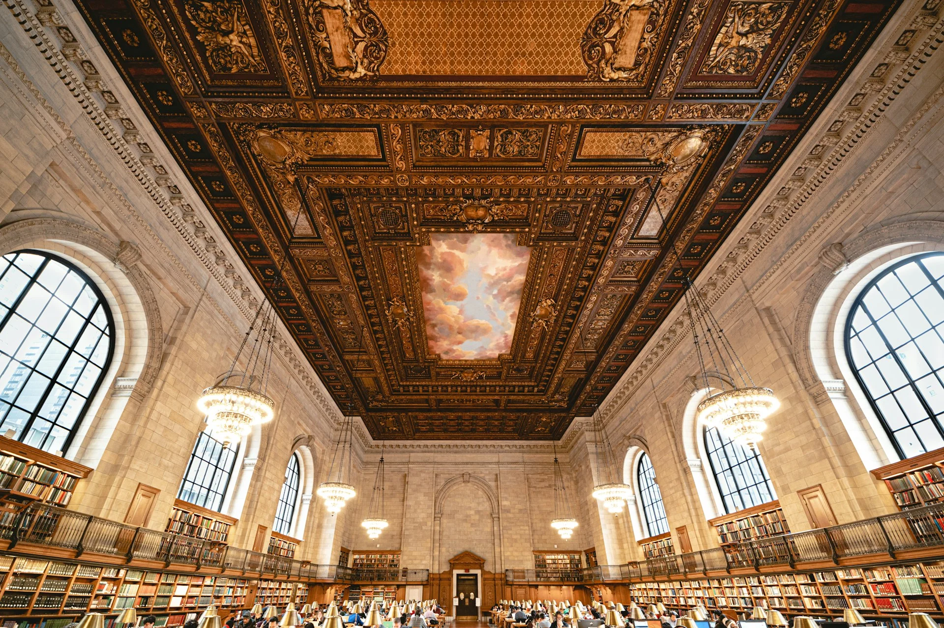 A grand public library reading room with long tables and arched windows