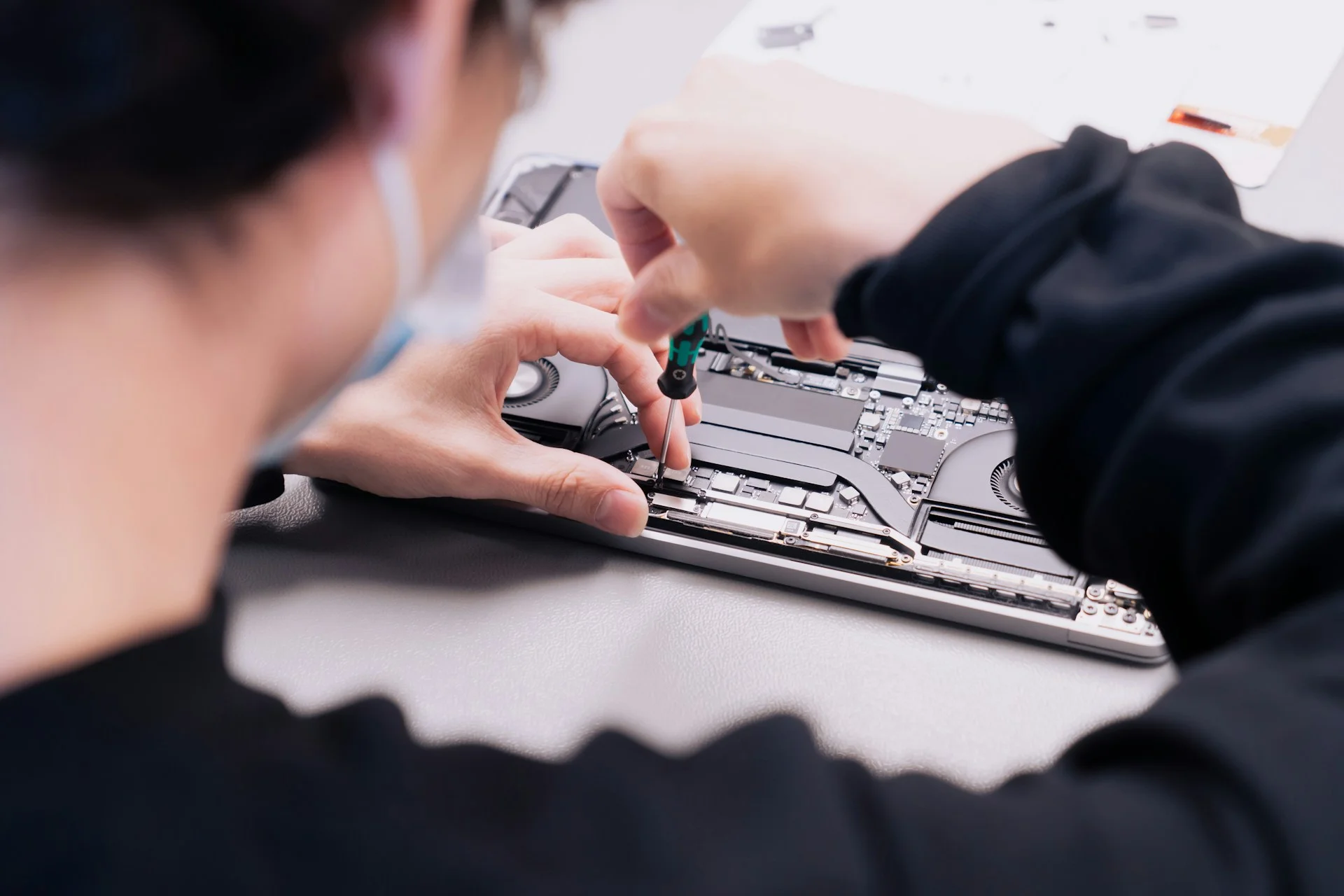 A repair bench with a disassembled laptop and tools, illustrating refurbished and second-hand computing hardware