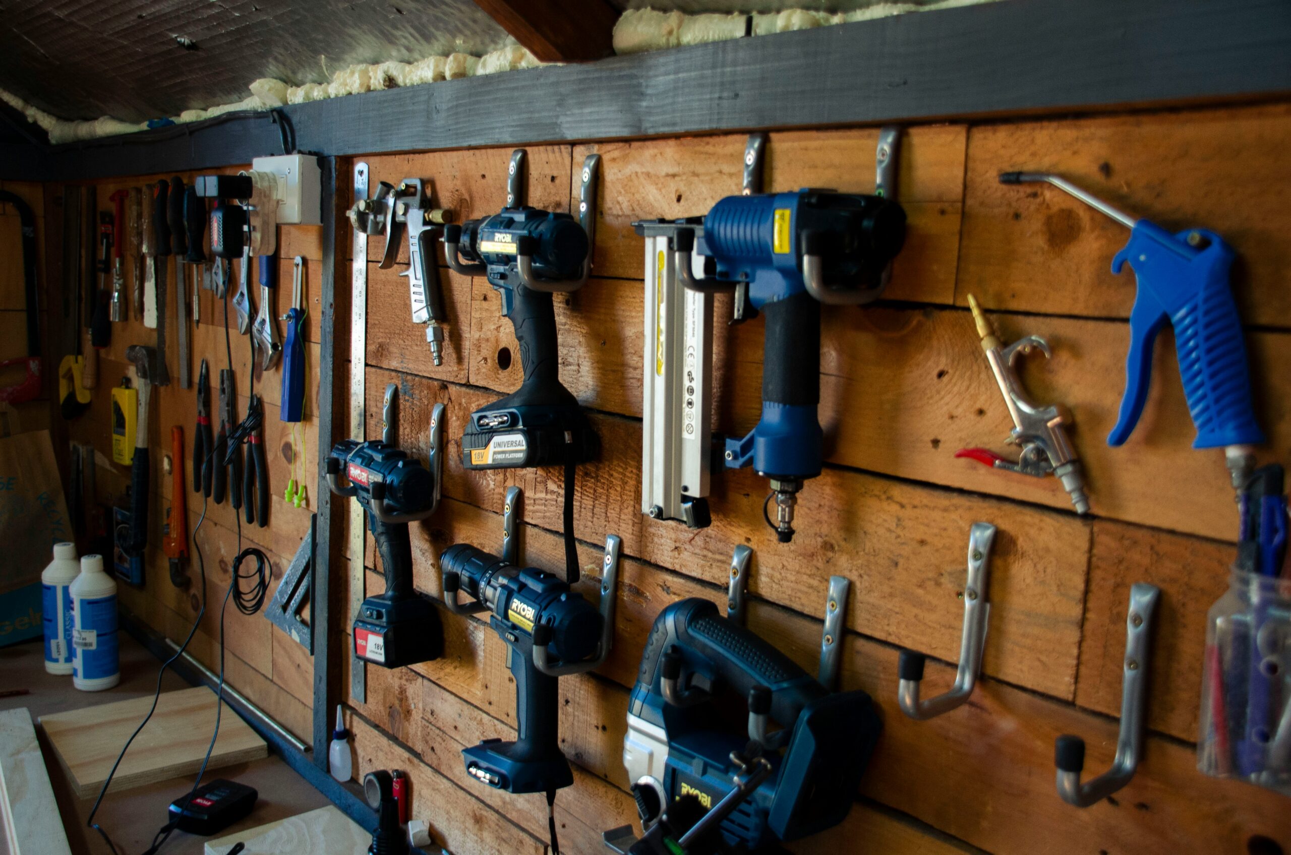 Power drills and hand tools hanging on hooks against a rustic community workshop wall